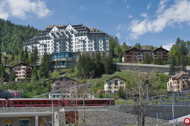 A luxurious Swiss hotel situated amidst lush green hills with a scenic railway running beneath, encapsulating serene alpine beauty.
