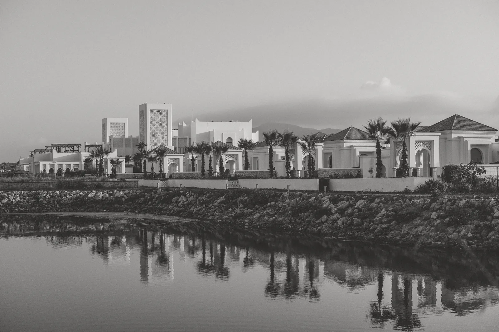 Black and white photo of modern Moroccan architecture by a calm waterfront in Fnideq, Morocco.