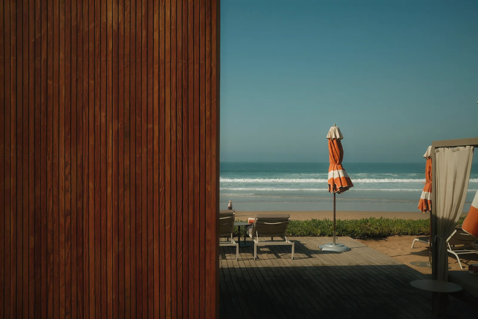 Peaceful beachfront setting in Morocco with deck chairs and closed orange umbrellas, perfect for relaxation.