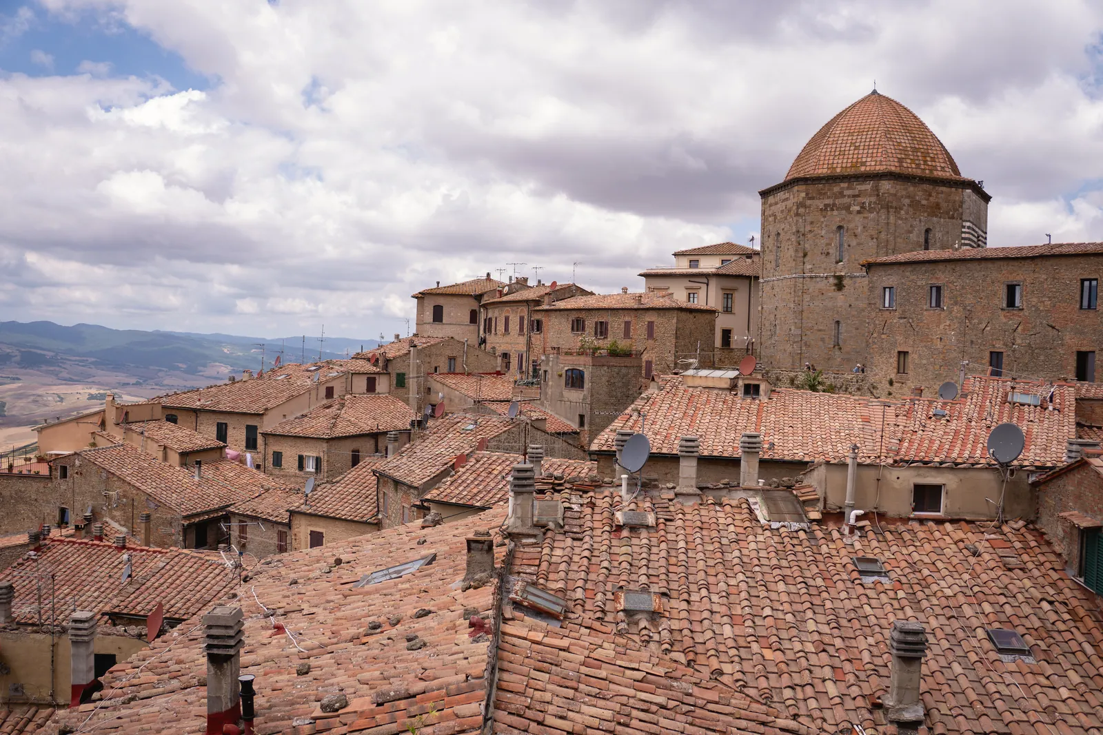 Explore the picturesque rooftops of a historic Italian village under a canvas of clouds.