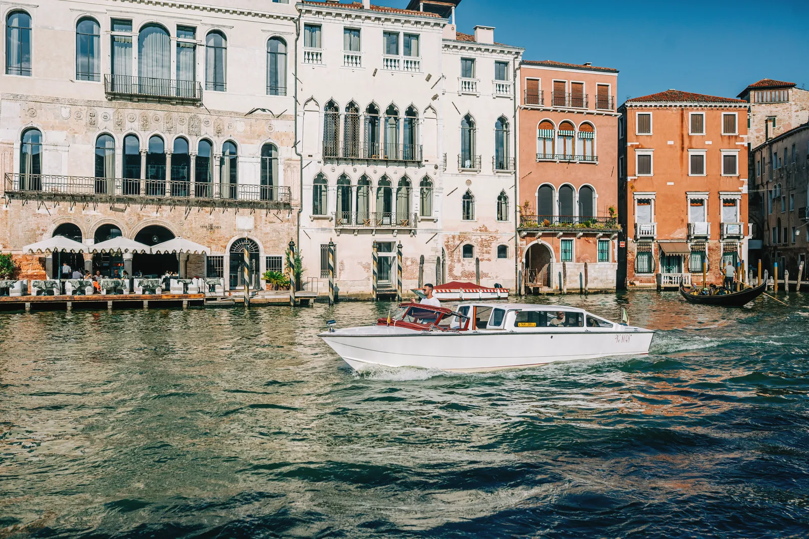 A water taxi navigates a picturesque canal in Venice, with historic Italian architecture lining the waterfront.