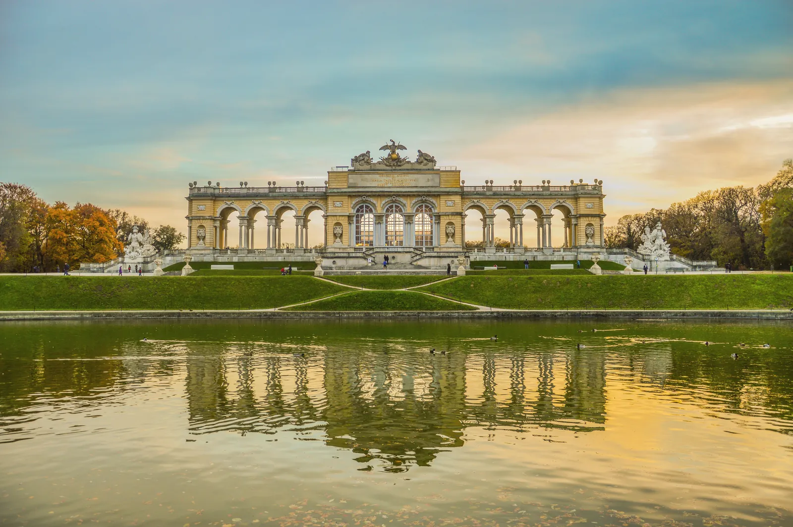 A stunning view of Schönbrunn Palace's Gloriette reflecting in a tranquil pond at sunset.