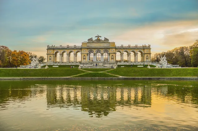 A stunning view of Schönbrunn Palace's Gloriette reflecting in a tranquil pond at sunset.