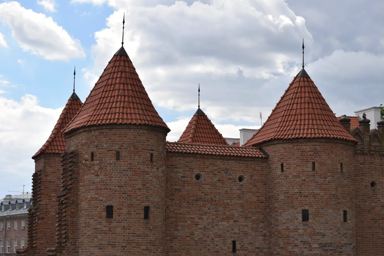 Majestic medieval brick towers of Warsaw Barbican against a partly cloudy sky.