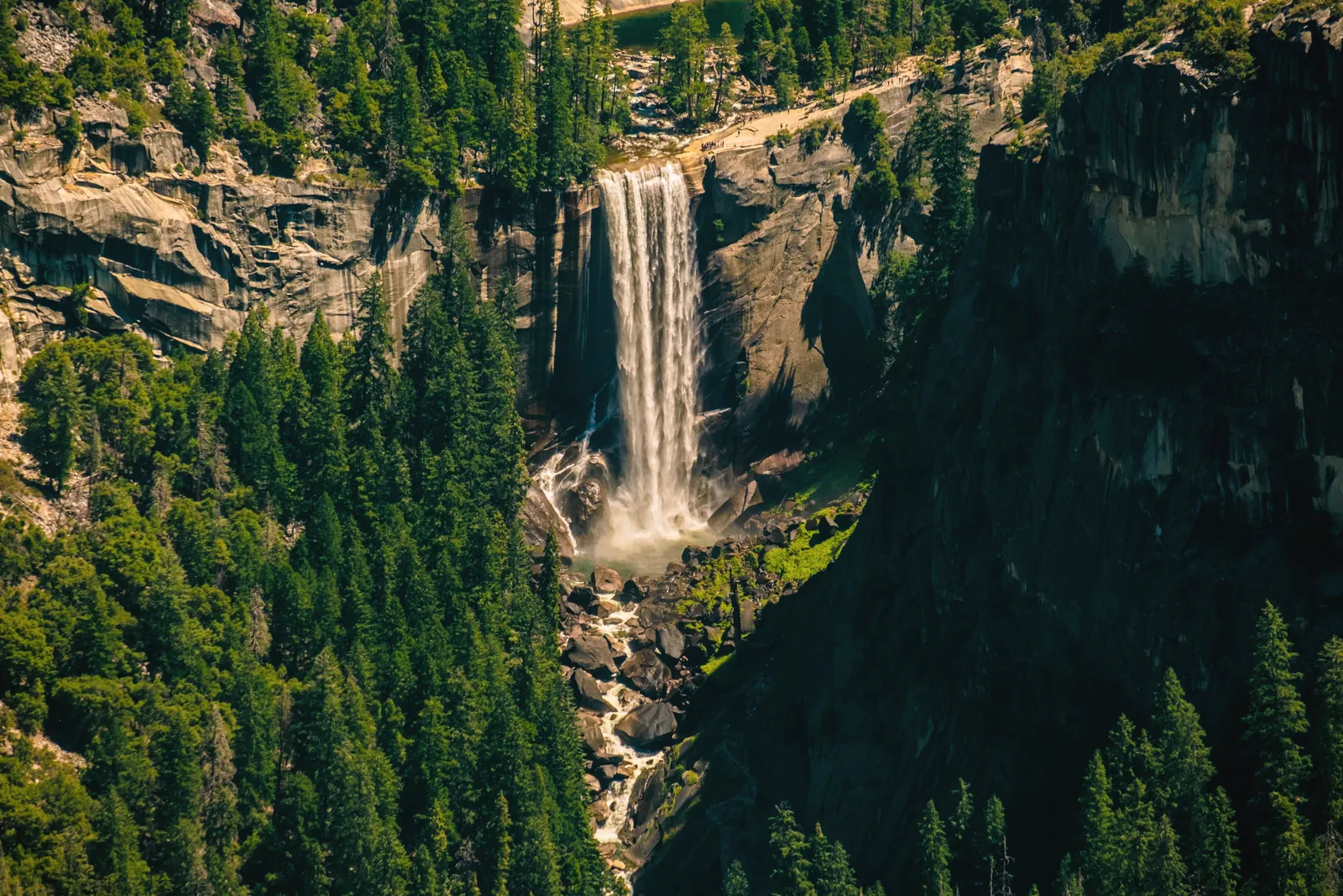 Stunning waterfall cascading down a cliff in Yosemite Valley, surrounded by lush greenery.