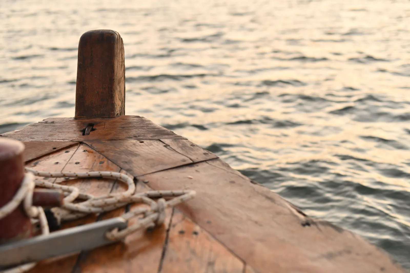 Close-up of a wooden boat bow with rope, sailing on calm wavy water.
